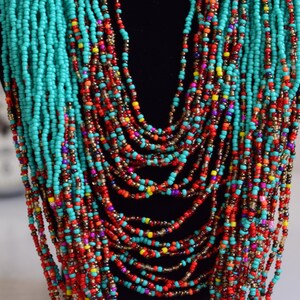 Puede incluir: Un collar de cuentas de m&uacute;ltiples hilos con cuentas turquesa, rojas, naranjas, amarillas y moradas. El collar est&aacute; en capas y cuelga en la parte delantera del cuello.