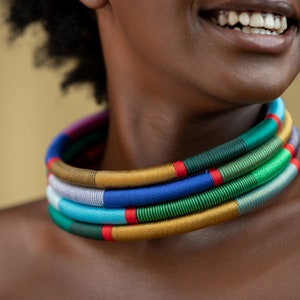 Puede incluir: Un collar de múltiples hilos con una vibrante gama de colores, incluyendo dorado, azul, verde y rojo. El collar está envuelto con hilos coloridos y es una pieza audaz. Un accesorio llamativo.