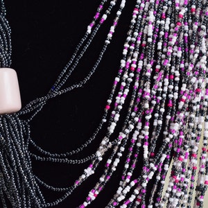 May include: A multi-strand necklace made of black, white, and pink beads. The necklace has a large, light pink bead at the top.