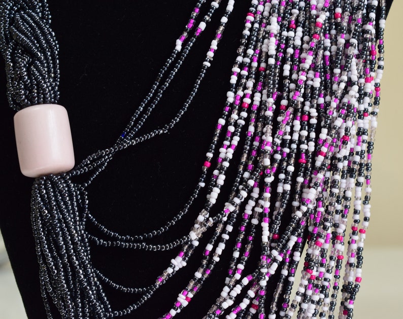 May include: A multi-strand necklace made of black, white, and pink beads. The necklace has a large, light pink bead at the top.