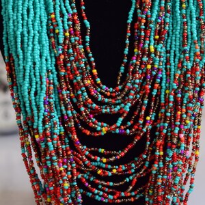 Puede incluir: Un collar de cuentas de m&uacute;ltiples hilos con cuentas turquesa, rojas, naranjas, amarillas y moradas. El collar est&aacute; en capas y cuelga en la parte delantera del cuello.
