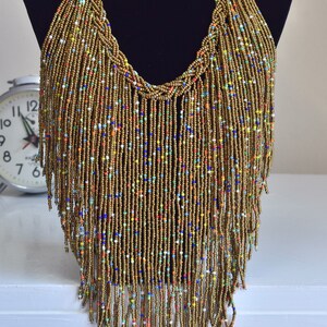 May include: A long, gold beaded necklace with a fringe of colourful beads. The necklace is displayed on a black mannequin.