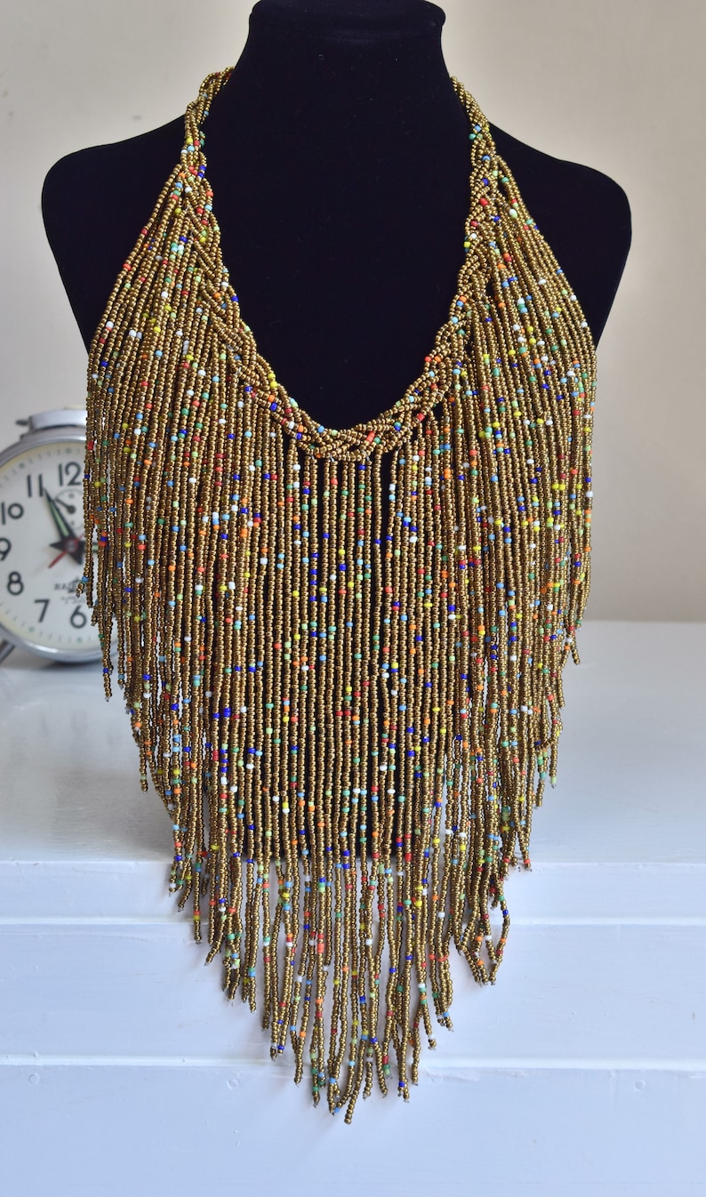 May include: A long, gold beaded necklace with a fringe of colourful beads. The necklace is displayed on a black mannequin.
