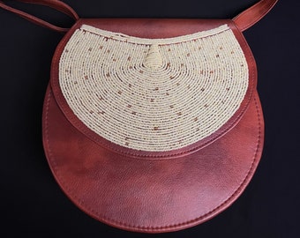 May include: A brown leather crossbody bag with a white beaded flap. The bag is circular in shape and has a long strap.