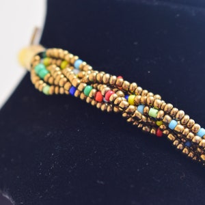 May include: A braided necklace with gold and multicoloured beads. The beads are small and round, and the necklace is woven in a tight pattern.