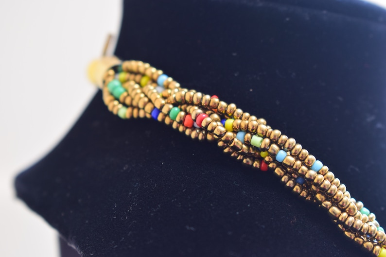 May include: A braided necklace with gold and multicoloured beads. The beads are small and round, and the necklace is woven in a tight pattern.