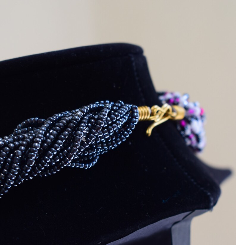 May include: A black beaded necklace with a gold clasp. The necklace is on a black velvet display stand.