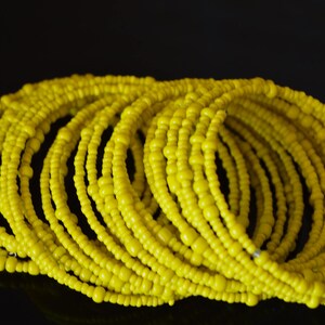 May include: A stack of yellow beaded bracelets. The bracelets are made of small, round beads that are strung together to form a continuous loop.