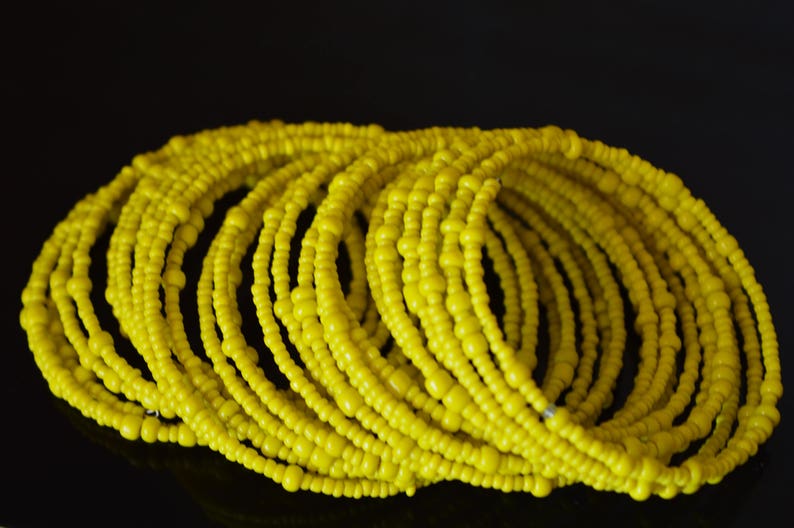 May include: A stack of yellow beaded bracelets. The bracelets are made of small, round beads that are strung together to form a continuous loop.