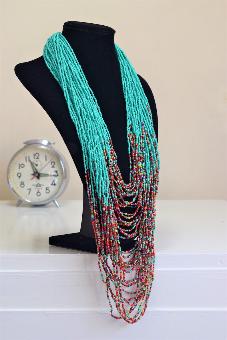 Puede incluir: Un collar largo de cuentas turquesa y multicolor con un dise&ntilde;o graduado. El collar se muestra en un maniqu&iacute; negro.