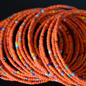 May include: A close-up of a stack of orange beaded bracelets with small colorful beads interspersed throughout.
