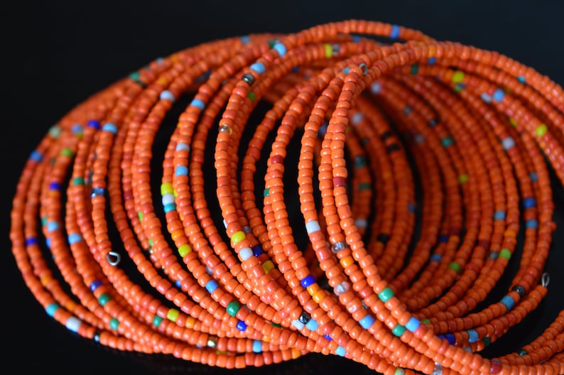May include: A close-up of a stack of orange beaded bracelets with small colorful beads interspersed throughout.