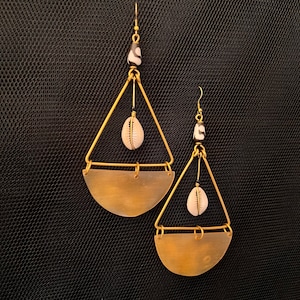 May include: A pair of gold earrings with a geometric triangle design. Each earring features a small white seashell charm and a black and white bead.