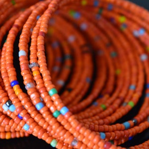 May include: A close-up of a beaded necklace made of orange, blue, and green beads. The necklace is made of many strands of beads, creating a layered effect.