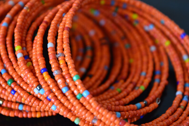 May include: A close-up of a beaded necklace made of orange, blue, and green beads. The necklace is made of many strands of beads, creating a layered effect.