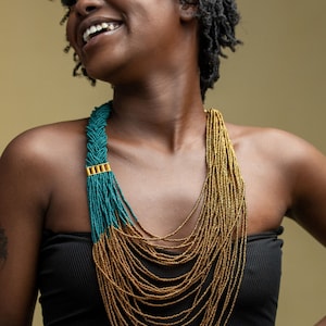 May include: A woman wearing a black strapless top with a long, layered necklace made of gold and teal beads.