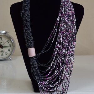 May include: A long, multi-strand necklace made of black, white, and pink beads. The necklace is draped over a black mannequin and features a pink bead accent.