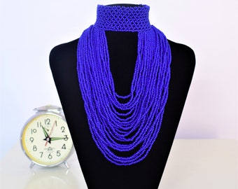 May include: A long, layered necklace made of small, blue beads. The necklace is displayed on a black mannequin bust. The necklace is about 18 inches long and has a choker style top.