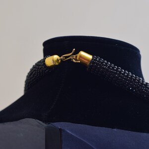 K&ouml;nnte beinhalten: Eine schwarze Perlenkette mit einem goldenen Verschluss. Die Kette wird auf einer schwarzen Samt-B&uuml;ste pr&auml;sentiert.