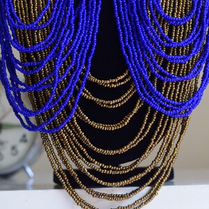 May include: A long, layered necklace made of blue and gold beads. The necklace is draped over a black mannequin.
