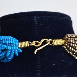 May include: A close-up of a gold-toned clasp connecting two strands of beads. One strand is turquoise blue and the other is a darker brown.