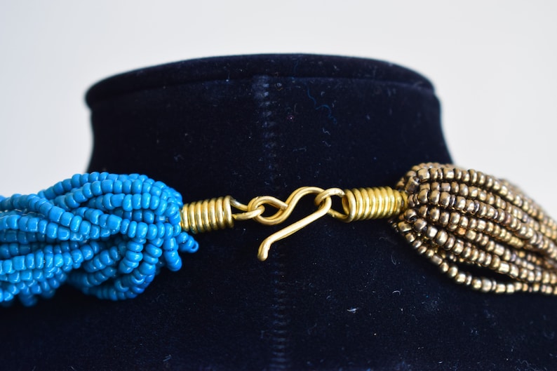 May include: A close-up of a gold-toned clasp connecting two strands of beads. One strand is turquoise blue and the other is a darker brown.