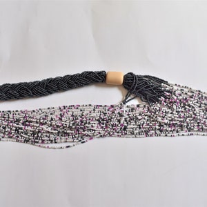 May include: A long, multi-strand necklace made of small white, black, and purple beads. The necklace is braided and has a wooden bead accent.