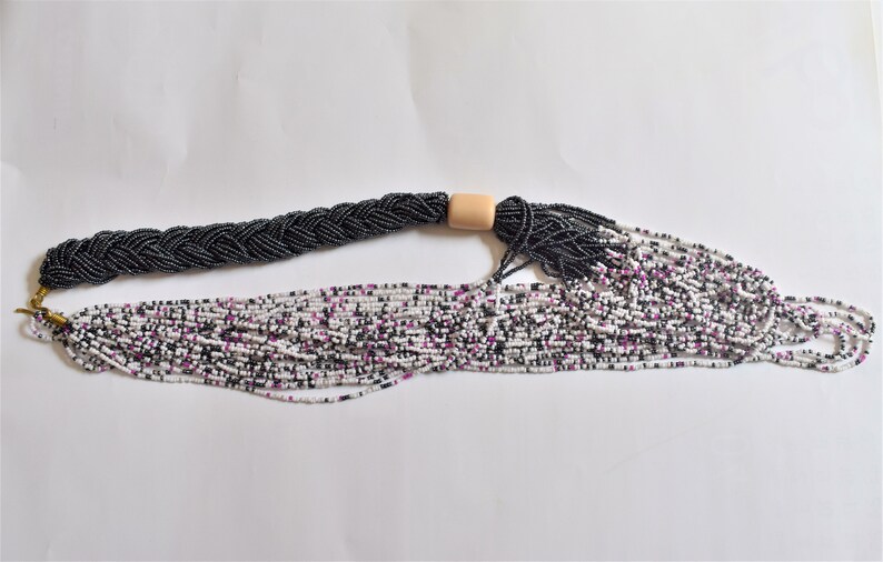 May include: A long, multi-strand necklace made of small white, black, and purple beads. The necklace is braided and has a wooden bead accent.