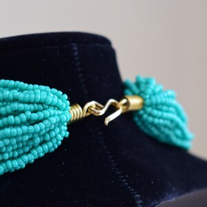 Puede incluir: Un collar de cuentas turquesa con un cierre dorado. El collar est&aacute; hecho de muchos hilos de cuentas peque&ntilde;as.