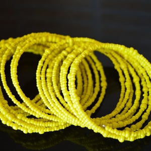 May include: A stack of yellow beaded bracelets. The bracelets are made of small, round beads that are strung together to form a continuous loop.