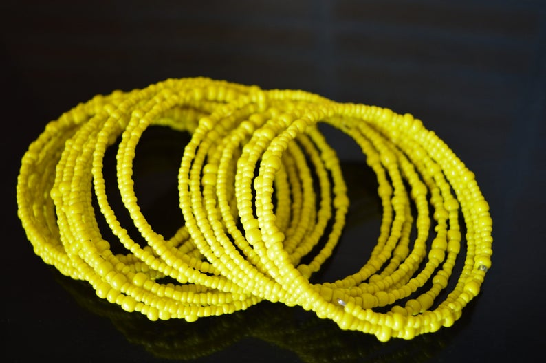 May include: A stack of yellow beaded bracelets. The bracelets are made of small, round beads that are strung together to form a continuous loop.