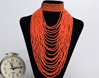 May include: A long, layered necklace made of orange beads with gold accents. The necklace is displayed on a black mannequin bust.