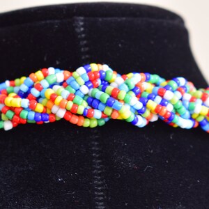 May include: A multi-colored beaded necklace with a braided design. The necklace is made of small, round beads in shades of red, orange, yellow, green, blue, and white.