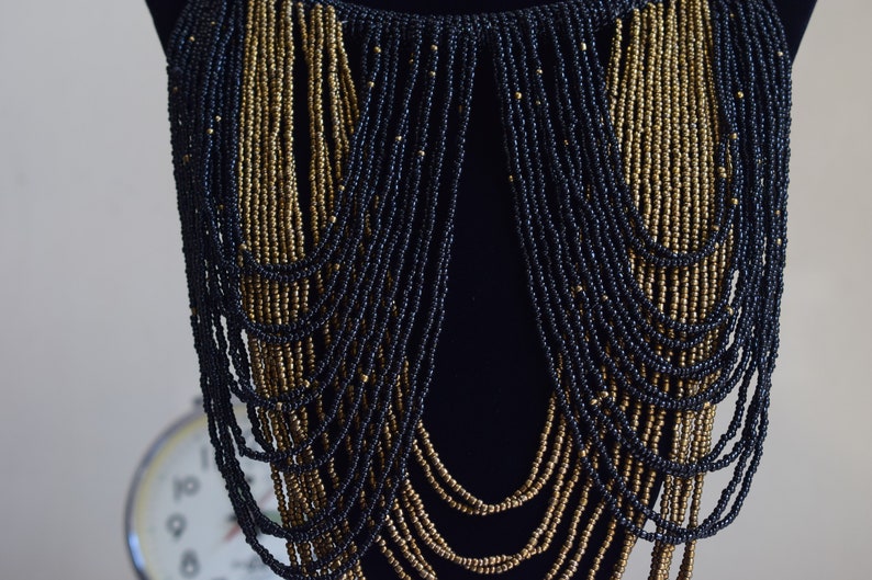 K&ouml;nnte beinhalten: Eine lange, mehrreihige Halskette aus schwarzen und goldenen Perlen. Die Halskette ist &uuml;ber einen schwarzen Mannequin-Busen gelegt.