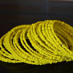 May include: A stack of yellow beaded bracelets. The bracelets are made of small, round beads that are strung together in a continuous loop.