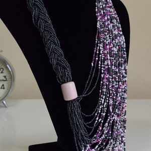 May include: A long, layered necklace made of black, white, and pink beads. The necklace is displayed on a black velvet bust form.