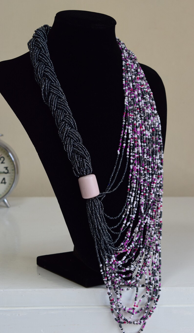 May include: A long, layered necklace made of black, white, and pink beads. The necklace is displayed on a black velvet bust form.