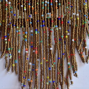 May include: A beaded fringe necklace with a brown base and colourful accents. The fringe is made of small, round beads in various colours, including red, blue, green, yellow, and white.