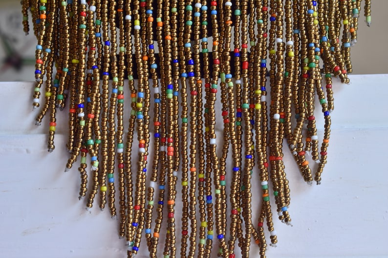 May include: A beaded fringe necklace with a brown base and colourful accents. The fringe is made of small, round beads in various colours, including red, blue, green, yellow, and white.