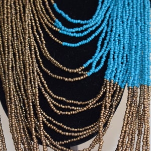 May include: A long, layered necklace made of small, gold and turquoise beads. The necklace is arranged in a cascading pattern, with the turquoise beads at the bottom.