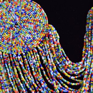 May include: A colorful beaded necklace with a large circular pendant. The necklace is made of small, brightly colored beads in a variety of shades of blue, green, red, yellow, and white. The pendant is a spiral of beads that creates a circular design.