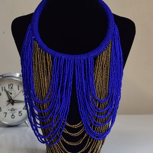 May include: A long, layered necklace made of blue and gold beads. The necklace is displayed on a black mannequin bust.