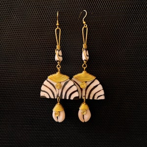 May include: A pair of long, gold-toned earrings with a black and white shell design. The earrings have a dangling shell charm at the bottom.