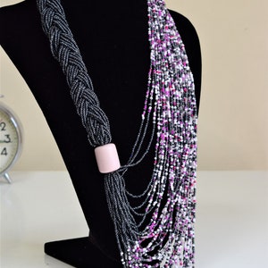 May include: A long, layered necklace made of black, white, and pink beads. The necklace is braided at the top and has a pink bead accent.