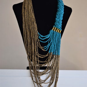 May include: A long, layered necklace with brown and turquoise beads. The necklace is made of multiple strands of beads, with the turquoise beads forming a braided design at the top. The necklace is displayed on a black mannequin.