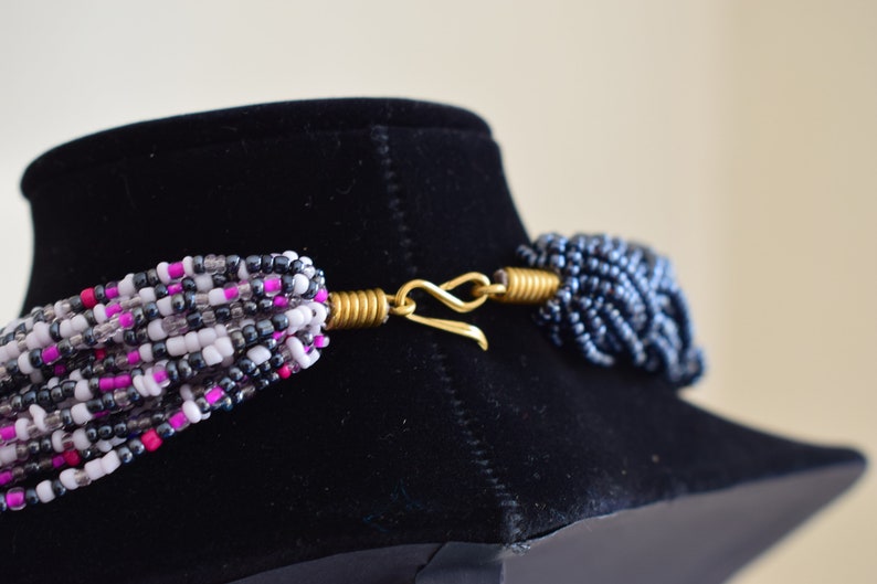 May include: A multi-strand necklace with pink, white, and gray beads. The necklace has a gold clasp.