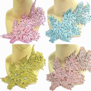 May include: Four floral lace appliques in pink, light blue, gold, and rose gold. Each piece features layered petals with a glittery finish and a central rhinestone accent. The designs include intricate leaf and vine patterns in a cluster arrangement.