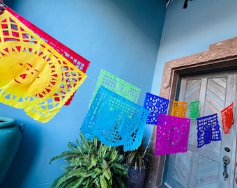 May include: A string of colorful paper banners with intricate cut-out designs. The banners are strung together and hanging from a wall. The banners are in the colors yellow, red, blue, green, purple, and orange.