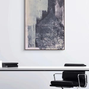 May include: A modern office setting featuring a white desk with black metal legs, a black leather office chair, and an abstract painting in shades of gray and white. The room has a minimalist design.