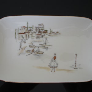 May include: A white porcelain dish with a gold rim features a hand-painted scene of a small town with buildings, boats, and people. The scene is painted in shades of brown, green, and gray.